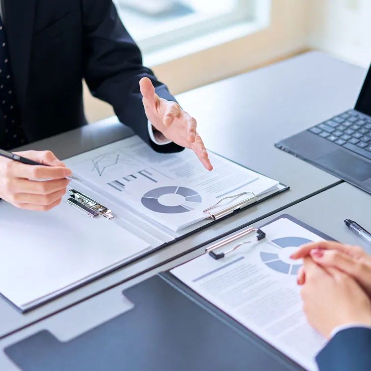 ビジネス資料を広げながらクライアントに提案内容を説明する担当者の手元