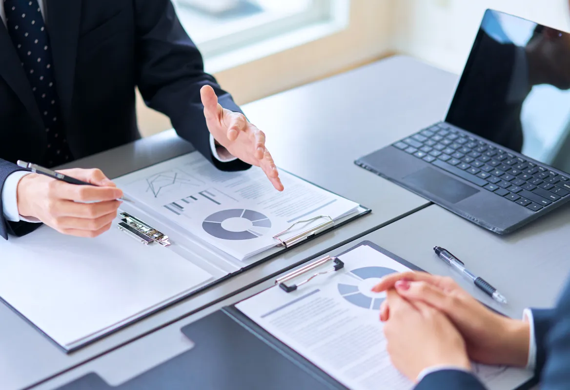 ビジネス資料を広げながらクライアントに提案内容を説明する担当者の手元