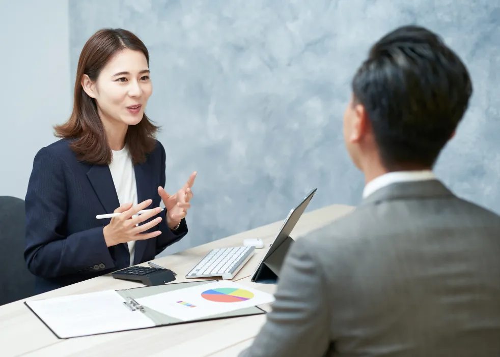 女性職員が机の対面にいる男性のお客様に説明している様子