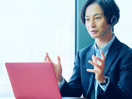 ヘッドセットを装着した男性職員がオンライン会議でノートPC画面に向かって説明している様子